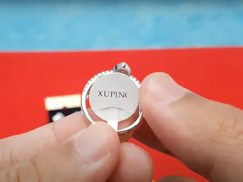 برچسپ لوگوی برند XUPING متصل به یک انگشتر نقره‌ای رنگ از زیورآلات ژوپینگ