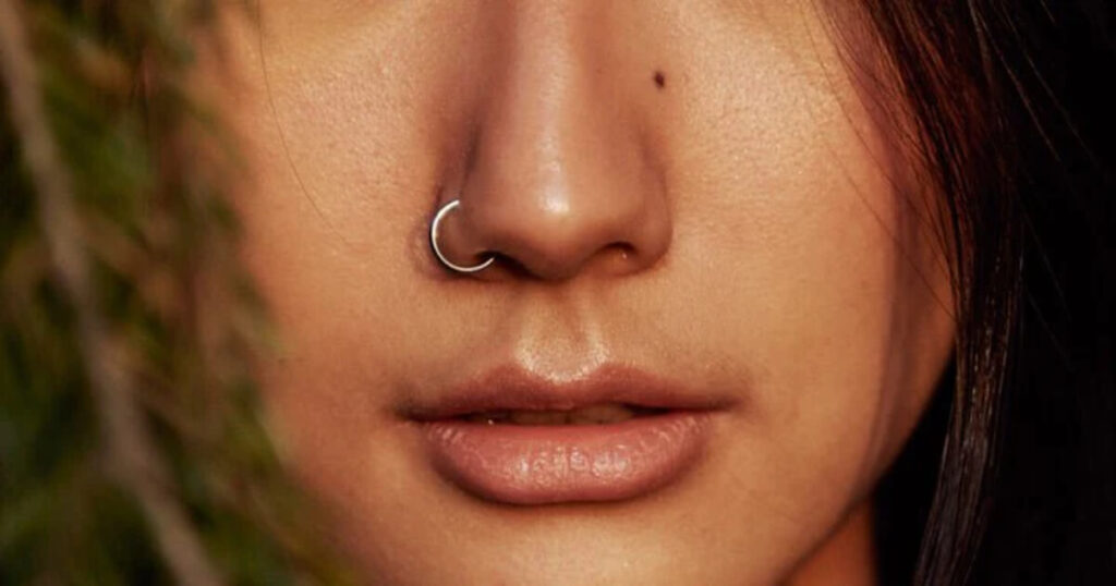 پیرسینگ بینی سمت چپ با حلقه نقره‌ای ساده روی صورت زن جوان