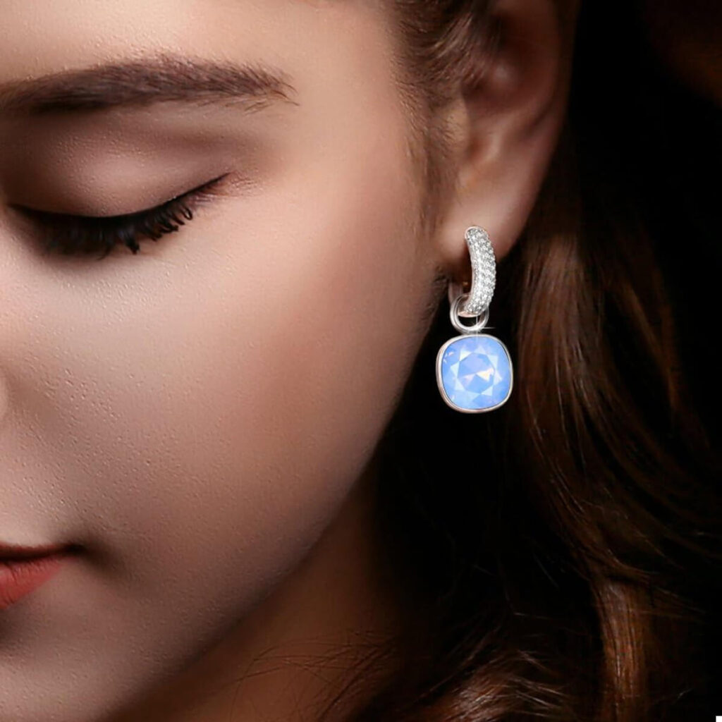 گوشواره ژوپینگ نقره ای با نگین های ریز و یک نگین بزرگ آبی روی گوش یک دختر جوان